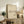 May include: Minimalist line drawing of a dachshund dog in black ink on cream textured paper, attributed to Picasso, displayed in light wood frame on rustic wooden sideboard alongside fern plant, ceramic vases, and stacked books in neutral-toned living room setting