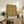 May include: Framed vintage botanical pattern poster with intricate golden yellow and brown floral damask design displayed on rustic wooden sideboard alongside fern plant, ceramic vase, books, and cream upholstered armchair in warm, naturally lit living room setting.