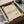 A minimalist line drawing of a dachshund in black ink on beige textured paper, signed "Picasso" in cursive script. The artwork is displayed in a black frame inside an open cardboard shipping box with protective tissue paper and wooden corner guards visible around the packaging.