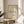 May include: Framed line drawing of a dachshund in simple black strokes on cream textured paper, displayed on a round wooden side table next to a beige upholstered chair. Natural sunlight streams across the minimalist room with white walls and a plant visible in the corner.