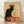 May include: Framed vintage French poster print featuring a black cat with arched back and flowing tail, sitting against cream background with ornate circular design behind its head. Red and orange text reads "Tournée du Chat Noir" and "Rodolphe Salis" with "Prochainement" at top. Art Nouveau style illustration in wooden frame, leaning against white wall on light wooden floor.