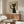 May include: Framed poster of black cat holding wine glass on beige background, displayed above wooden credenza in modern living room with white curved chair, glass coffee table, and minimalist decor