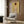 May include: Framed reproduction of Egon Schiele artwork showing figure with red hair from behind, draped in white fabric against yellow background. Modern living room setting with beige upholstered chair, geometric patterned pillow, gold floor lamp, dark round side table with open book, and wood paneled wall.