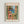 May include: Framed poster print featuring a colorful Mediterranean coastal scene viewed through green shuttered windows. The artwork shows coral-pink buildings with a palm tree, blue ocean with small boats, and tropical plants in the foreground. The print has "MATISSE" at the top and "VIEW OF NICE" at the bottom in terracotta lettering, displayed in a light wood frame against a white wall.