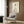May include: Framed artwork showing a sleeping cat in Japanese ink wash style with black calligraphy text, displayed above a cream upholstered armchair with geometric patterned pillow. Modern reading corner features brass floor lamp and dark round side table with open book. Warm wood paneled wall and white curtains create cozy atmosphere.