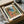 May include: Framed art print featuring a colorful Mediterranean coastal scene with coral-pink buildings, green shutters, palm trees, and turquoise water viewed through an open window. The vintage-style poster shows "MATISSE" and "VIEW OF NICE" text. Black frame sits in cardboard shipping box with protective tissue paper wrapping.