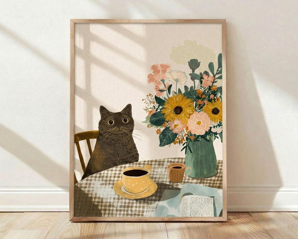 May include: Framed art print showing a gray tabby cat sitting at a table with checkered tablecloth, yellow coffee cup, wooden mug, open book, and large floral bouquet with sunflowers and pink blooms in green vase. Natural wood frame leaning against white textured wall on light wooden floor with diagonal window shadows.