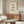 May include: Framed poster with cream background featuring a cute calico cat with black and white patches sitting contentedly with closed smiling eyes, accompanied by black Japanese calligraphy characters and small red seal stamp. Artwork is displayed above a mid-century modern walnut credenza with brass hardware in a minimalist living room setting with white curved chair, glass-top oval coffee table, and neutral decor.