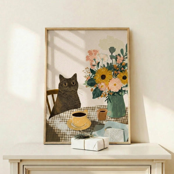 May include: Framed poster print on light wooden shelf showing black cat with golden eyes sitting at checkered tablecloth table with yellow coffee cup, colorful flower bouquet in green vase featuring sunflowers and pink blooms, open book, all in cozy illustrated art style. Small wrapped gift with sprig sits on shelf beside frame against cream wall with natural window lighting.