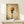 May include: Framed kitchen wall art showing spaghetti noodles twirled on a black fork against a vintage sepia background with soft clouds. The golden pasta appears to drip slightly from the fork tines. Displayed on a light wood shelf next to a small wrapped gift box with twine and greenery sprig. The frame has a thin natural wood border and the overall style is realistic with warm, muted tones.