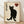 May include: Framed poster print featuring a black cat silhouette with golden eyes sitting upright against a cream textured background. Vertical Japanese kanji characters appear on the left side, with a red heart containing a black kanji character in the upper right. The artwork is displayed in a light wood frame, leaning against a white wall on wooden flooring with soft natural lighting creating shadows.