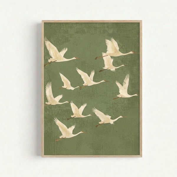 A framed art print featuring nine white cranes in flight against a sage green textured background. The birds are arranged in a scattered formation with outstretched wings and long necks, rendered in a minimalist style with cream and pale yellow tones. The artwork is displayed in a simple light wood frame against a white wall.