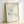 May include: Minimalist line drawing of a stretching cat in black ink on cream paper, displayed in a light wood frame leaning against a white wall. The simple, continuous line artwork shows a cat in a downward stretch pose with flowing tail, signed with "Picasso" in the lower right corner.