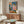 May include: Picasso's 1905 Two Acrobats artwork displayed above a walnut credenza in a modern living room. The painting shows two figures in harlequin costumes - one in diamond-patterned clothing, one in pink - against blue and coral backgrounds. White sculptural chair and glass-top coffee table complete the mid-century modern interior with warm wood tones and neutral walls.