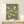 May include: Framed poster with green background showing nine white cranes in flight, displayed on light wood console table next to small wrapped gift with evergreen sprig. Natural wood frame, soft lighting creates gentle shadows on cream wall behind.