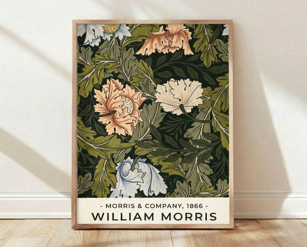 May include: Framed botanical art print featuring William Morris-style pattern with large blooming flowers in peach, white, and pale blue against dark green foliage background. Light wood frame displayed on wooden floor against white wall with soft natural lighting creating subtle shadows.