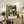May include: Framed botanical poster with green foliage and pink, white, and coral flowers displayed on rustic wooden sideboard alongside fern plant, ceramic vases, and books in neutral-toned living room setting with beige chair and lamp visible.