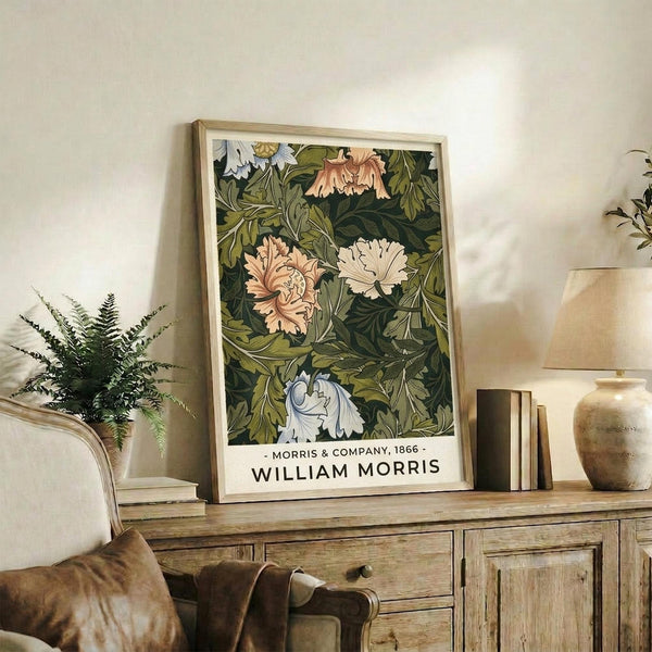 May include: Framed botanical poster with green foliage and pink, white, and coral flowers displayed on rustic wooden sideboard alongside fern plant, ceramic vases, and books in neutral-toned living room setting with beige chair and lamp visible.