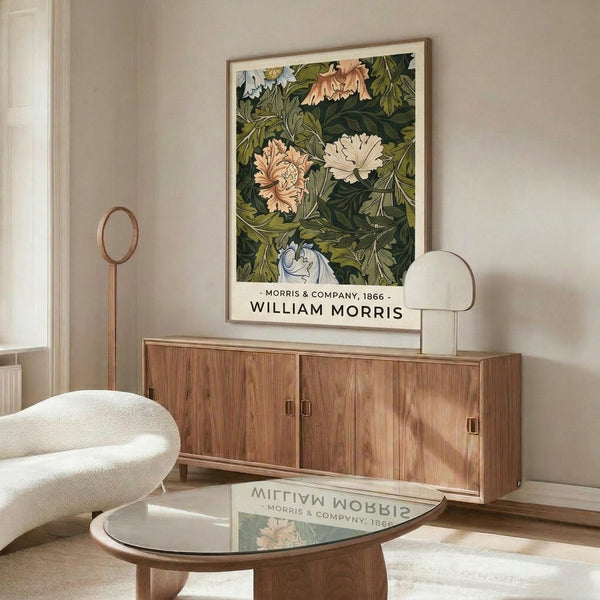 May include: Framed botanical print featuring William Morris floral design with pink, white and blue blooms on dark green foliage background, displayed above wooden sideboard in modern living room with cream walls, white upholstered chair, glass coffee table, and warm natural lighting creating shadows on polished floor.