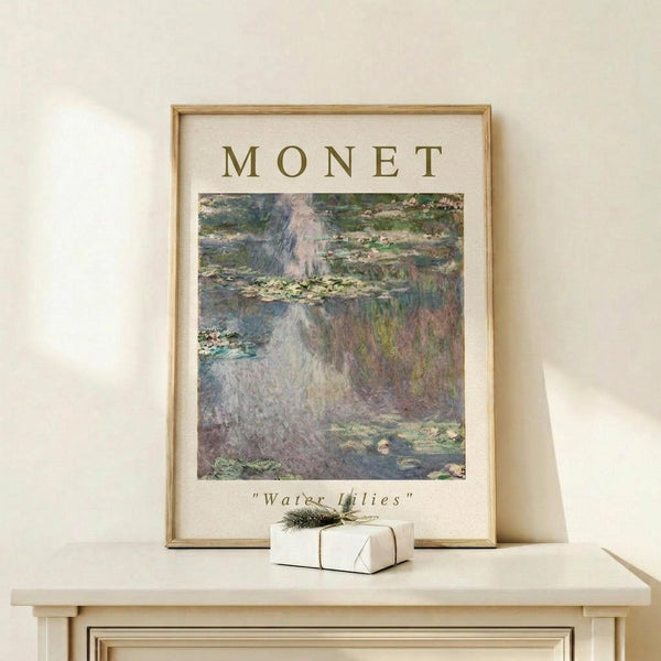 May include: Framed art print of Monet's Water Lilies painting featuring impressionist brushstrokes in soft blues, greens, and purples depicting lily pads floating on reflective pond water. Print displays "MONET" at top and "Water Lilies" at bottom in elegant typography. Light wood frame sits on pale wooden shelf beside small white wrapped gift with evergreen sprig against cream wall with natural lighting.