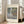 May include: Framed art print of Monet's Water Lilies painting displayed in bright living room with cream walls, beige sofa, and natural lighting. The poster features soft impressionist brushstrokes in muted greens, purples, and yellows depicting lily pads floating on reflective water. Text reads "MONET" at top and "Water Lilies Claude Monet, 1877" at bottom on cream background within light wooden frame.