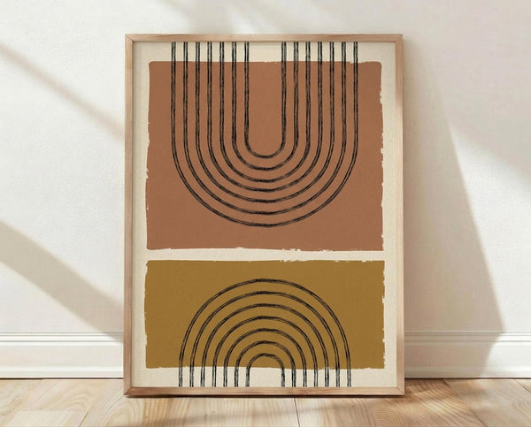 May include: Framed geometric art print featuring two stacked rectangular sections - upper terracotta section with black concentric arches forming an upside-down rainbow pattern, lower mustard yellow section with black concentric arches in traditional rainbow formation. Light wood frame with white matting, leaning against white wall on natural wood flooring with soft shadow patterns.