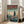 May include: Framed poster displayed in bright living room with beige sofa and large windows. Artwork shows futuristic pilot in spacesuit standing on rooftop overlooking cyberpunk cityscape with tall buildings. Japanese text at top, teal and orange color scheme with rainy atmosphere. Light wood frame leaning against white wall on hardwood floor.
