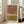 May include: Modern abstract art print displayed in light wood frame on floor next to beige sofa in bright living room. Artwork features geometric rainbow arches in black lines on terracotta orange and mustard yellow color blocks with white background. Natural sunlight streams through tall windows creating shadows on white walls and hardwood floors.