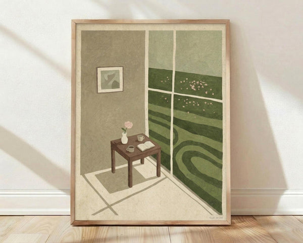May include: Framed art print leaning against white wall on wooden floor. Artwork shows cozy interior corner with brown table holding pink flower vase, teacup and open book. Large window reveals rolling green hills dotted with small white flowers under pale sky. Small framed artwork hangs on olive-colored wall. Soft natural lighting creates gentle shadows across the scene.