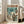 May include: Framed anime-style poster showing armored figure with umbrella walking through rainy neo-Tokyo street with giant mecha silhouette looming in background, displayed in bright living room with beige sofa, white walls, and large windows casting natural light across wooden floors.