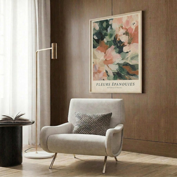 May include: Light beige armchair with geometric pillow positioned against wood-paneled wall. Above hangs framed botanical art print featuring abstract floral brushstrokes in soft pink, coral, green and cream tones. Gold floor lamp and dark round side table with open book visible nearby. Warm natural lighting creates cozy modern interior setting.
