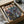 May include: Framed anime-style poster featuring two armored figures in a rainy cyberpunk cityscape with neon lighting, displayed in black frame inside cardboard shipping box with protective packaging materials on wooden surface