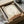 May include: Framed surrealist poster print featuring a large pale circular moon or sun with subtle botanical impressions against a cream background, with a tiny silhouetted figure walking along a terracotta orange horizon line. Black frame sits in cardboard packaging with tissue paper and shipping materials on white surface.