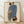 May include: Framed poster print leaning against white textured wall on light wood floor with natural shadows. Shows minimalist illustration of figure from behind wearing blue striped top, holding brown handbag, with leopard print pants. Artwork has cream background in natural wood frame.