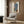 May include: Modern beige armchair with geometric pillow in contemporary room setting. Abstract fashion artwork on wood-paneled wall shows minimalist figure in blue striped top and leopard print shorts holding brown clutch. Gold floor lamp and dark round side table with open book complete the neutral-toned interior scene.