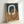 Abstract geometric artwork featuring two interlocking rounded rectangular rings in cream and terracotta orange colors. The background is split horizontally between deep navy blue on top and warm beige textured paper below. The piece is displayed in a thin natural wood frame, leaning against a white wall with soft shadows visible.