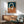 May include: Abstract modern poster with interlocking oval rings in cream, terracotta orange, and navy blue colors, displayed in wooden frame above mid-century credenza. Scene shows mint green upholstered armchair with wooden arms, white ceramic table lamp, and warm natural lighting creating shadows on white wall.