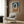 May include: Abstract art print with interlocking oval rings in navy blue, terracotta orange, and cream colors, displayed in light wood frame on wood paneled wall above beige upholstered armchair with geometric patterned pillow, brass floor lamp, and dark side table with open book in modern living room setting