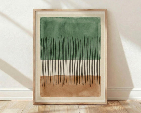 May include: Framed abstract watercolor artwork leaning against white wall on light wood floor. The piece features vertical black brushstrokes resembling tall grass or reeds emerging from brown earth at bottom and green foliage wash at top. Natural wood frame with cream matting, soft shadows cast on textured white wall from window light.