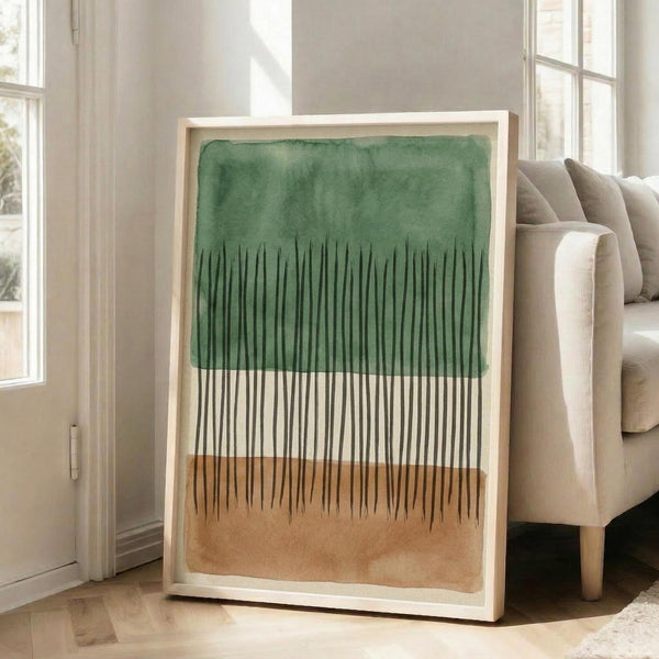 May include: Framed abstract artwork with green watercolor wash at top, vertical black lines creating grass-like texture, and warm beige wash at bottom. Light wood frame displayed against white wall next to beige upholstered sofa in bright living room with large windows and natural light.