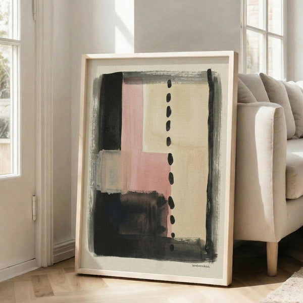May include: Large framed abstract art print leaning against white wall next to beige sofa in bright living room. Artwork features brushy geometric shapes in pink, cream, charcoal and black with vertical dotted line through center. Natural wood frame on hardwood floors with sunlight streaming through tall windows.