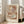 May include: Abstract geometric art print in warm earth tones featuring overlapping translucent circles and curved shapes in terracotta, sage green, cream, and dusty pink. The framed poster leans against a white wall next to a beige upholstered sofa in a bright, minimalist living room with large windows and natural light casting soft shadows on the floor.