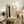 May include: Abstract art print in light wood frame displayed on rustic wooden console table beside fern plant and books. Artwork features soft pink watercolor blocks, black brushstroke, dotted line, and wavy line on cream background. Cozy living room setting with beige chair, throw blanket, and ceramic vases creating warm, modern home decor styling.