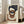 May include: Large framed abstract geometric art print leaning against white wall next to beige armchair in bright living room. Artwork features overlapping organic shapes in navy blue, terracotta brown, and cream on textured off-white background within light wood frame. Natural sunlight streams through tall windows creating soft shadows on hardwood floors.