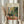 May include: Person in cream sweater holding framed Henri Matisse exhibition poster featuring colorful still life painting with teacup, plants, and window view. One hand also holds dried pampas grass stems. Neutral curtained background with soft natural lighting creates minimalist styling scene.