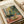 May include: Henri Matisse art print displayed on white surface next to beige ribbon. The colorful painting shows an interior scene with tropical plants, pottery, and a window, rendered in Matisse's characteristic bold brushstrokes using vibrant greens, yellows, pinks, and blues. The print appears to be from the National Gallery of Modern Art collection.