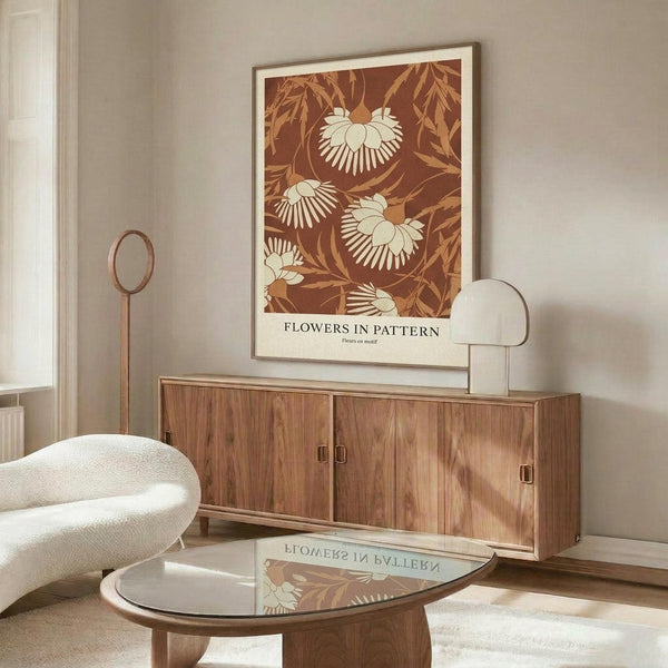 May include: Mid-century modern living room featuring a framed botanical poster with cream and rust-colored daisy-like flowers against a terracotta background. The print hangs above a walnut wood credenza with brass hardware. A white curved chair, brass floor lamp, glass-top coffee table, and neutral walls complete the warm, minimalist interior styling.