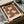 May include: Vintage-style botanical poster with cream and rust brown floral pattern featuring stylized flowers and leaves, displayed in black frame inside cardboard shipping box with protective tissue paper and wooden dowel tubes for packaging