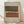 May include: Framed abstract geometric artwork with layered horizontal bands in dark brown, cream, and terracotta colors featuring dotted patterns, displayed in light wood frame against white textured wall on wooden floor with natural lighting creating soft shadows