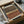 Framed abstract geometric art print featuring horizontal bands in brown, rust orange, cream, and beige tones with dotted halftone pattern overlay. The artwork is displayed in a black frame, carefully packaged in brown cardboard box with protective tissue paper and wooden dowels for safe shipping.
